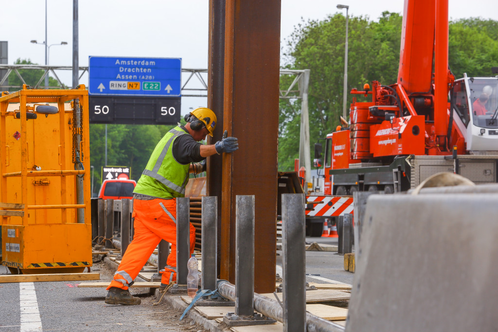 1 - Op de weg staan de heimachines. Tussen de rijbanen wordt een sleuf gemaakt. Hierin wordt de damwand gezet.