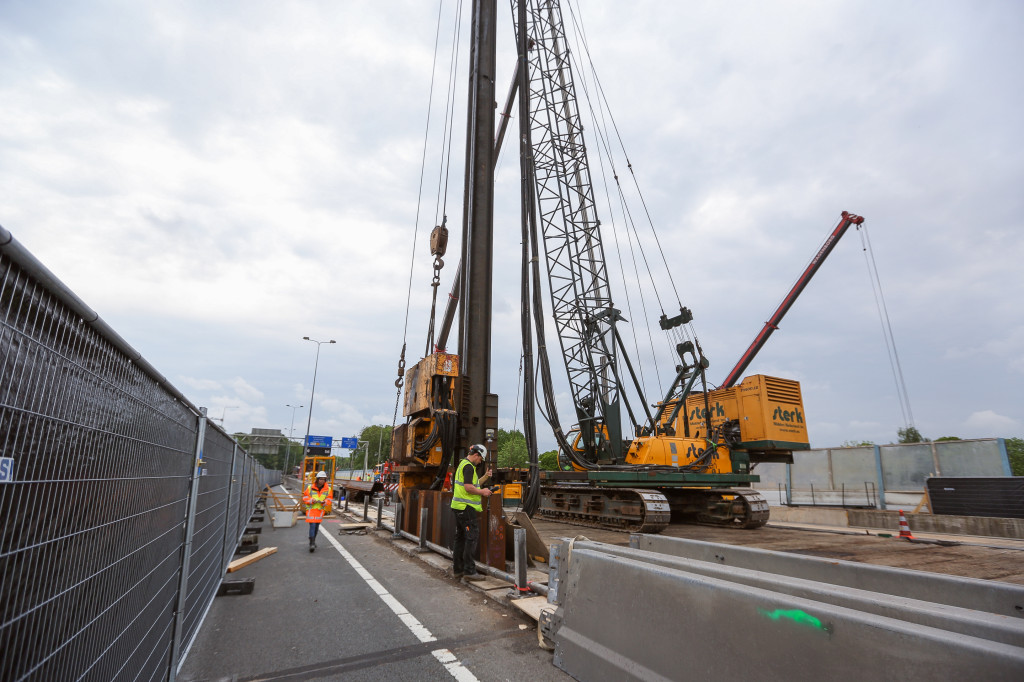 1 - Op de weg staan de heimachines. Tussen de rijbanen wordt een sleuf gemaakt. Hierin wordt de damwand gezet.